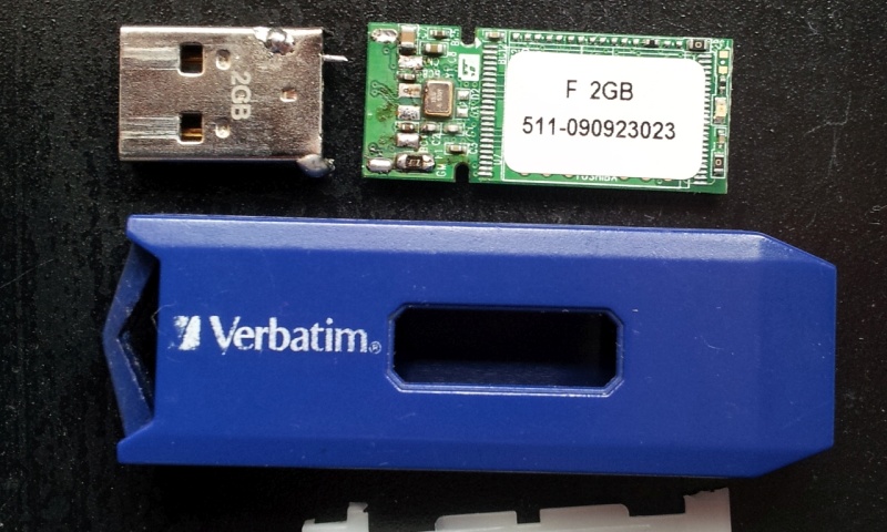 A Verbatim USB memory stick broken apart to show its internal circuit board. The silver usb connector is shown broken off the end and solder pads ripped off the pcb